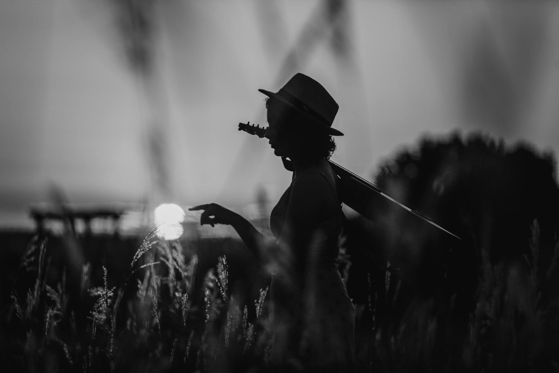 Black and white silhouette of a girl in a field with a guitar at sunset, evoking freedom and tranquility.