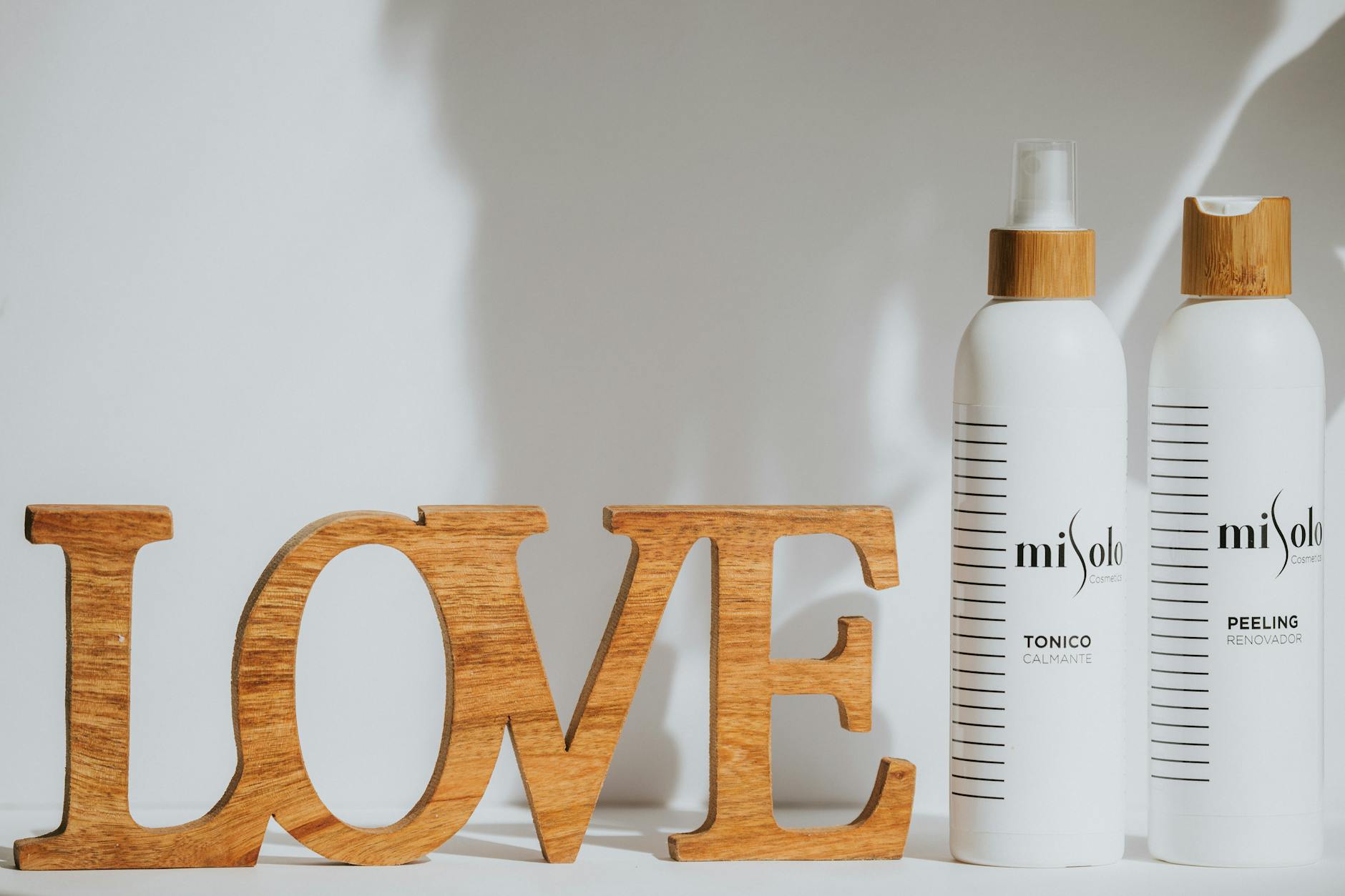 Stylish still life with Misolo skincare bottles and a wooden 'Love' sign on a neutral background.