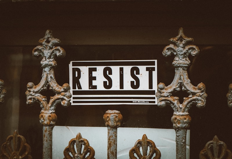 a rusted iron gate with a sign that reads resist