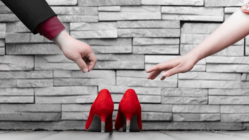 a pair of hands reaching for a pair of red high heels